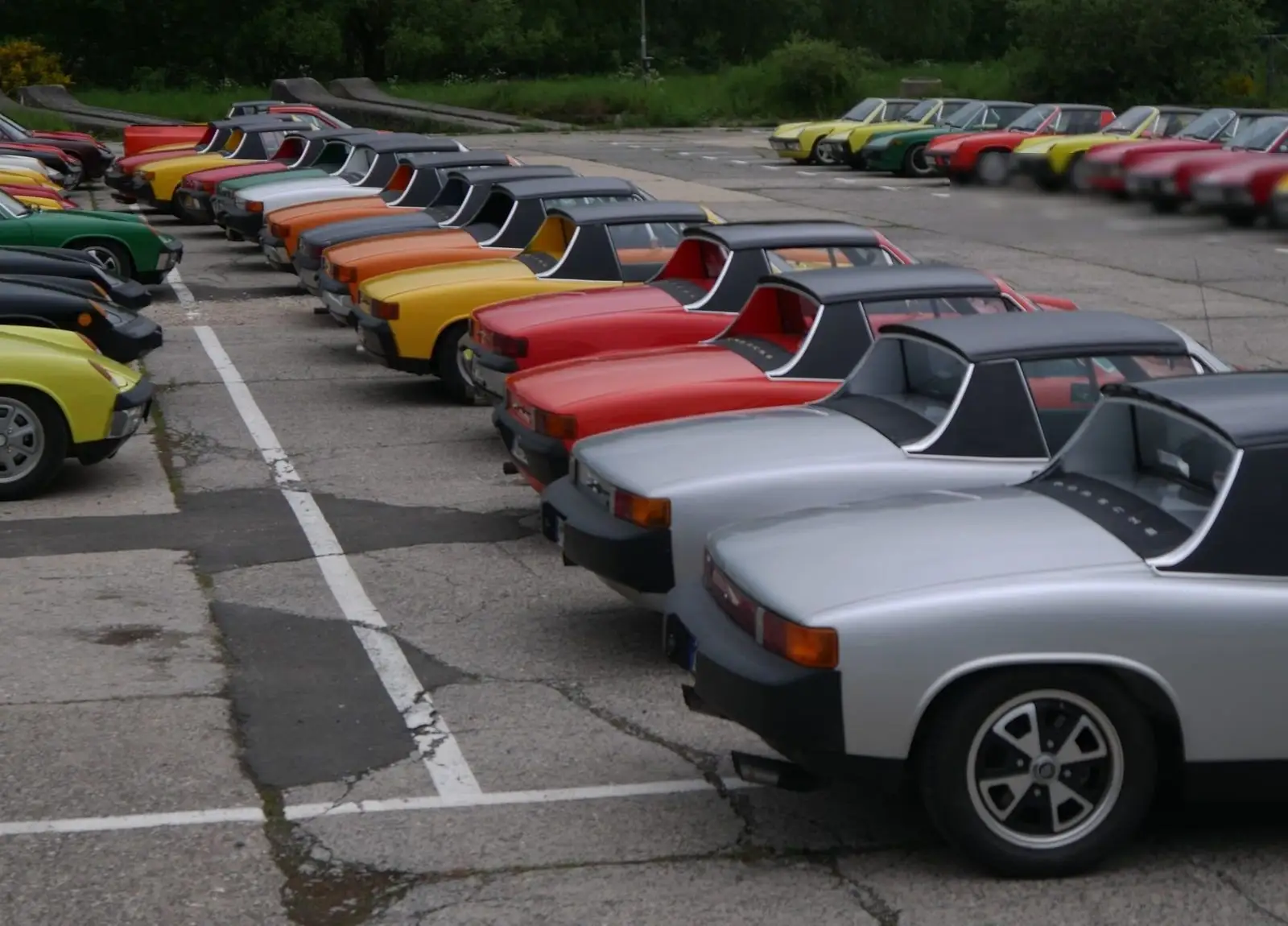 Porsche 914s in many colours lined up at an angle on a car park.